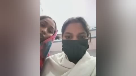 Media: Video of two South Asian women in surgical masks, one with a colorful headscarf, wearing white lab coats, standing in a hospital hallway.