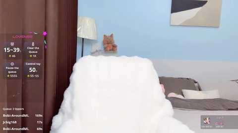 Media: Video of a cozy bedroom with a fluffy white blanket covering a bed, light blue walls, a cat toy, and a modern abstract painting.