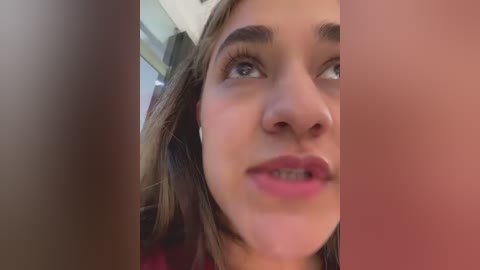 Media: Video of a young woman with light skin and brown hair, wearing pink lipstick, looking upwards, with blurred background.