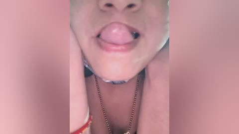A close-up video of a light-skinned woman's face, showing her slightly parted lips and tongue sticking out. She wears a silver necklace. The background is blurred, focusing on her face.