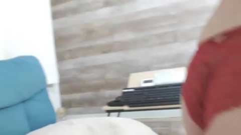 A video of a woman in a red shirt lying on a white bed with a blue cushion, with a beige brick wall and a white shelf with books in the background.