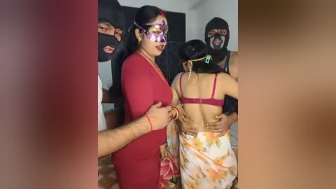 Video of a woman in a red dress and mask, surrounded by masked men, holding a woman in a floral saree, indoors with tiled floor.