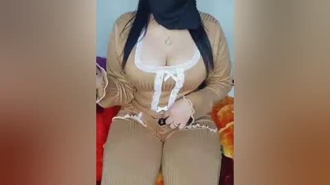 A video of a woman with fair skin, wearing a revealing, brown, ribbed knit top with a white bow revealing ample cleavage, sitting on a red cushioned surface.