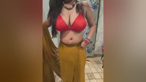 Video of a plus-sized woman with medium skin tone, wearing a red bra and mustard-yellow skirt, standing in a tiled bathroom with floral wallpaper.