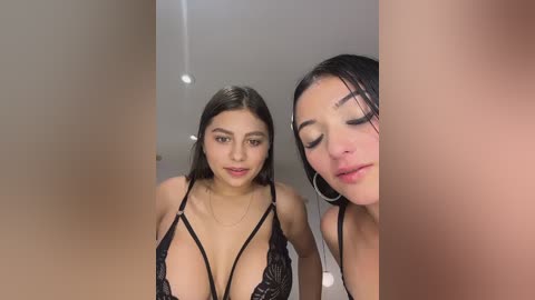 Video of a young Latina woman with long dark hair, wearing a revealing black lace lingerie top, posing in front of a mirror. She has fair skin, large breasts, and wears hoop earrings.