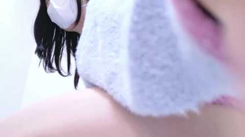 Close-up video of a woman with long, dark hair, wearing a white towel around her neck, blurred background.