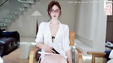 Video of a slender, fair-skinned woman with red hair, wearing glasses, a white blouse, and black lingerie, sitting on a wooden chair in a modern, minimalist living room with white walls and stairs.