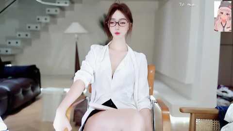 A young Asian woman with fair skin and red hair, wearing glasses, a white shirt, and black panties, sits on a modern chair in a minimalist living room with a staircase and plants in the background.