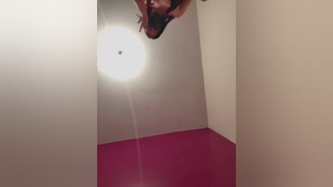 Video of a person with a dark complexion, wearing a black shirt, taking a selfie with a flash. The background is a plain white wall, and the floor is painted red.