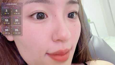 Video of a young Asian woman with fair skin, brown eyes, and straight brown hair, puckering her lips in a selfie. Background shows a calendar overlay and blurred bathroom setting.