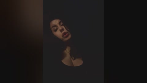 A video of a woman with dark hair, fair skin, and full lips, partially submerged in a dark, shadowy pool, creating a haunting, moody atmosphere.