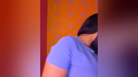 A video shows a person with long black hair wearing a blue shirt against an orange wall with a floral pattern, creating a vibrant and dynamic composition.