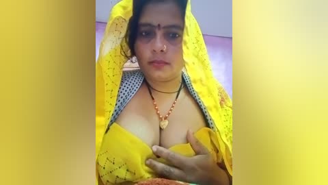 A video of a dark-skinned woman in a yellow sari, exposing her ample breasts, wearing a necklace, with a yellow background.