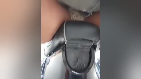 A video captures a close-up view of a woman's legs and crotch area, wearing tight, shiny black leather pants. Her skin tone is light, and the background is blurred, focusing on the texture of the leather and the woman's thighs.