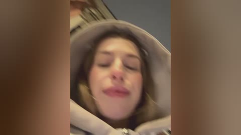 Video of a young woman with fair skin, closed eyes, and a relaxed expression, wearing a light-colored hoodie, partially obscured by blurred, out-of-focus foreground.