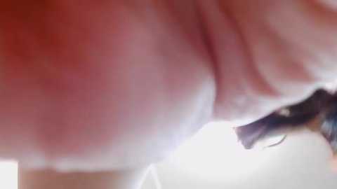 A close-up, blurry video of a human breast, with visible skin texture and slight redness, partially obscured by a dark-haired woman's hand, likely taken in a bathroom.