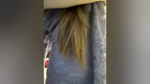A video showing a woman's long, straight, blonde hair cascading down the front of a light grey, lace-textured garment. The background is a neutral, blurred gradient.