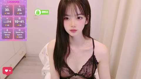 Video of an Asian woman with long black hair, wearing a black lace bra, in a minimalist room with a pink background.