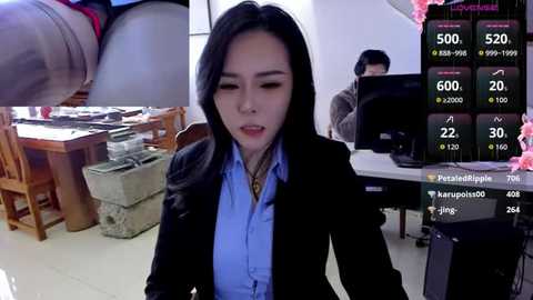Video: A Chinese woman in a black blazer over a blue shirt sits at a desk, looking at a monitor displaying financial data.