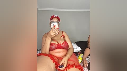 Video of a plus-sized Black woman with a red hat and lingerie, lying on a messy bed, holding a smartphone.