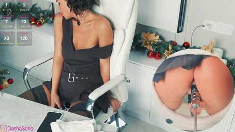 A video of a woman in a black off-shoulder dress, sitting on a white chair, revealing her bare buttocks with a metal object inserted. A festive Christmas tree decorates the background.