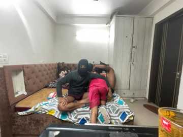 Media: Video of a small, dimly-lit room with a burglar in a hooded jacket, holding a gun, standing over a woman on a bed with another woman nearby, both in pink clothes.