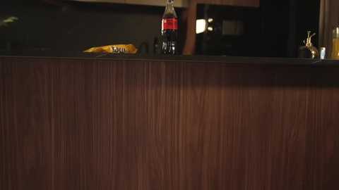 A video of a wooden bar counter with a Coke bottle, banana, and a partially visible glass in the background, dimly lit.