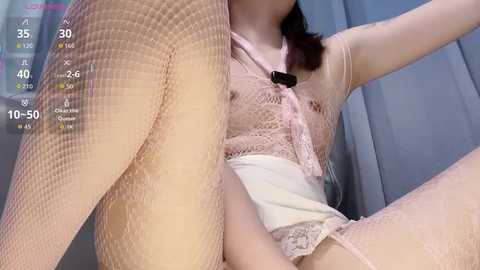 Video of an Asian woman in fishnet stockings and a lace top, sitting with legs spread, revealing her crotch.