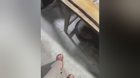 Video of a person's legs wearing red open-toed shoes and beige socks, standing in a dimly lit room with a wooden table and a metal chair in the background.
