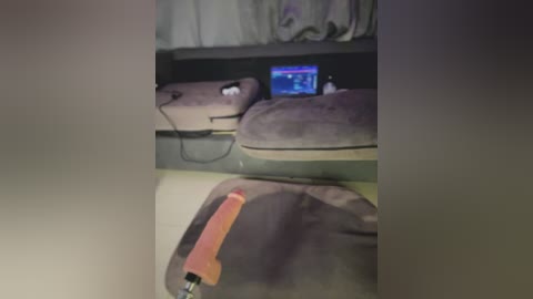 Video of a dimly-lit living room with a TV showing a game screen, a gray couch, and a large, orange dildo on a light-colored carpet.