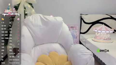 Video of a plush white armchair with a yellow cushion, adorned with a Christmas tree and a pink-and-white carousel toy, set in a minimalist room with a white and black patterned wall.