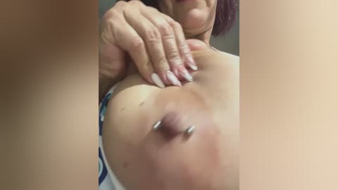 Video of a light-skinned woman with a large, pierced nipple, visible breasts, and manicured nails, partially obscured by her hand.