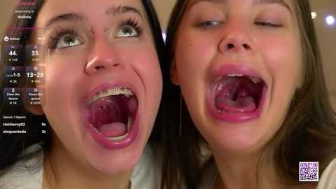 Video of two young women with braces, open mouths, and tongues visible. One has green eyes, the other brown. Background shows a video screen with stats.