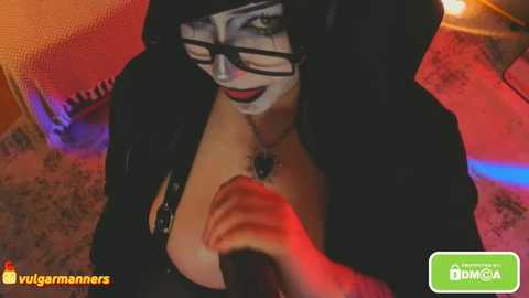 A video of a woman with pale skin, wearing a nun's habit, black glasses, and a black mask, holding her chest, in a dimly lit room with red and blue lighting.