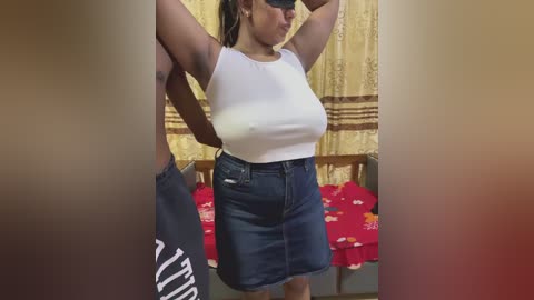 Video of a Black woman with medium skin tone, medium-sized breasts, and a slim figure, wearing a white crop top and dark blue denim skirt, posing in a room with red and yellow curtains.