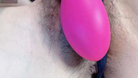 Video of a close-up view of a person's pubic area with a pink vibrator inserted. The person's pubic hair is visible and the skin tone is light.
