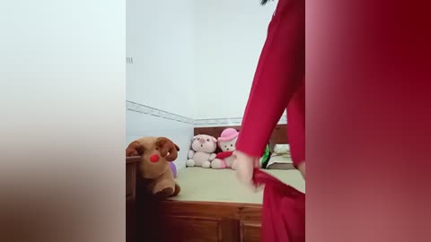 Video of a red-clad person walking in a room with a bed, wooden furniture, and plush toys, including a bear and a pink rabbit, in the background.