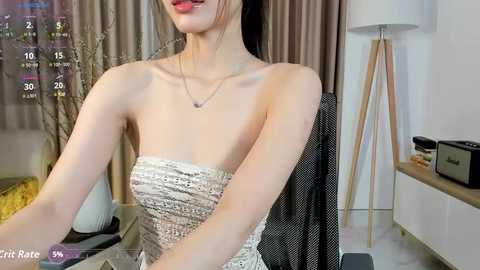 Video of a slender Asian woman with fair skin, wearing a strapless white lace dress, sitting at a desk in an office setting.