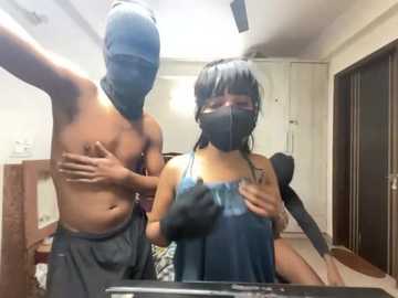 Video of a shirtless man in a blue mask, standing behind a woman in a blue mask and a blue dress, both in a dimly lit bedroom.