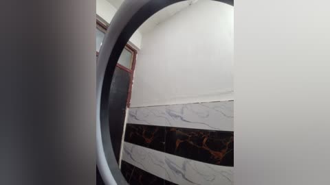Video of a small, dimly lit hallway with a black and white marble tiled floor and a white wall. A round mirror on the left reflects the hallway's ceiling and door frame.