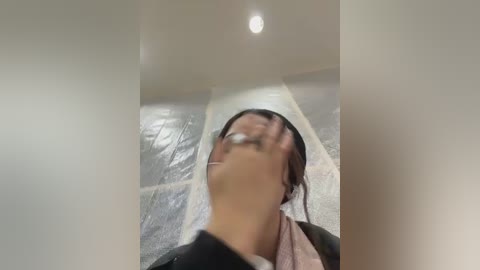 A blurry video of a person with dark hair and glasses, wearing a black jacket, lying on a white rug with a gray stone floor in the background.