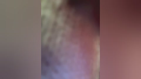 This image is a blurred video featuring a person in a dark outfit against a background with a mix of colors, including shades of brown, purple, and green. The subject's features are indistinguishable due to the lack of focus.