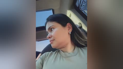 Video of a Latina woman with long dark hair, wearing a light green t-shirt, sitting in a car, looking out the window.