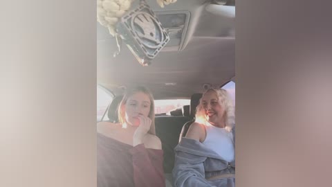 Media: Video of two young women, one with long blonde hair and the other with short brown hair, sitting in a car. They are holding cell phones, smiling, and wearing casual clothing.