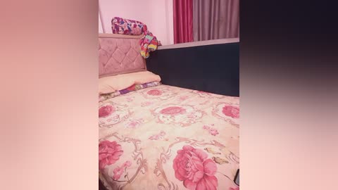 Video of a neatly made bed with a floral duvet in pink and beige, a quilted headboard, and colorful pillows. The room has pink curtains and a dark wooden frame.