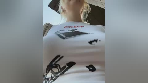 A video of a woman wearing a white t-shirt with a black abstract design and the word \"HIPP\" printed in red. Her blonde hair is tied back.