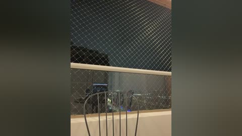 Video of a modern indoor scene featuring a black metal chair with a simple, curved backrest facing a large, reflective glass wall with a diamond-patterned metallic mesh. The background is dimly lit, creating a moody, industrial aesthetic.