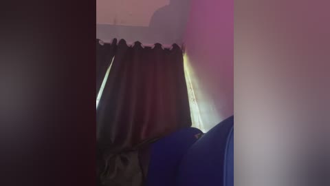 Video of a dimly lit room with a black curtain partially drawn, casting shadows. The background reveals a blurry, possibly outdoor scene with a hint of sunlight.