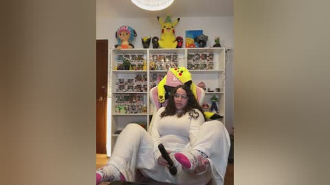 Video of a woman in a Pikachu costume sitting on a chair in a brightly decorated room with shelves full of Pokemon figurines.