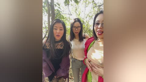 Video of three Asian women in a forest. One wears a purple jacket, another a beige top, and the third a red scarf. They stand together, smiling. Background shows trees and sunlight.